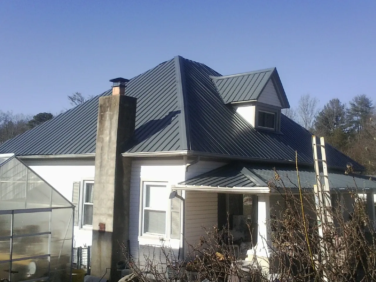Dark blue standing seam metal roof on a white farmhouse with dormer — Slate & Tile Roof Repair by Roofing Brothers in Prospect Park