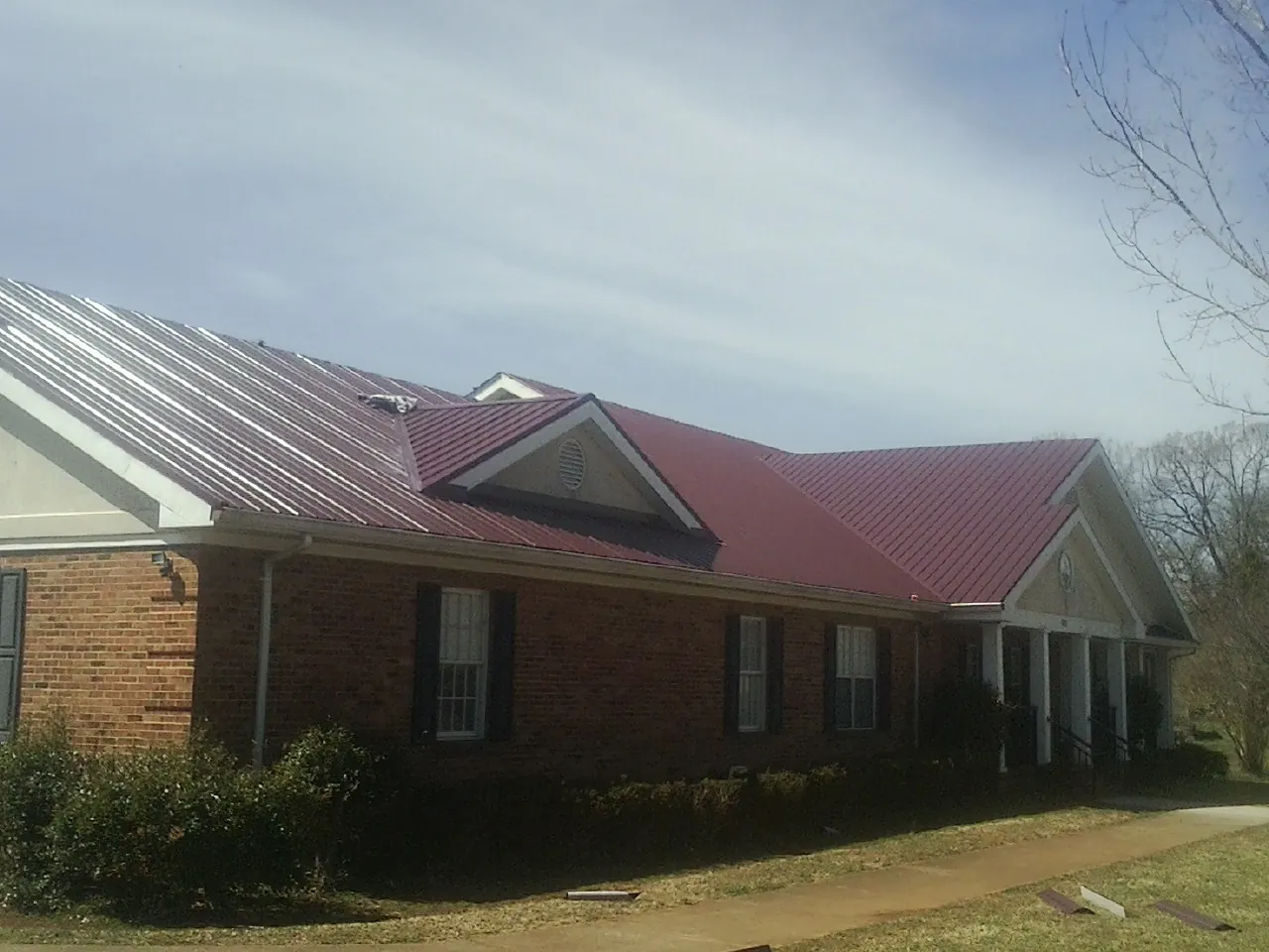 Red metal roof with gabled entries on a long brick building, from a Hail Damage Roof Repair job in Prospect Park