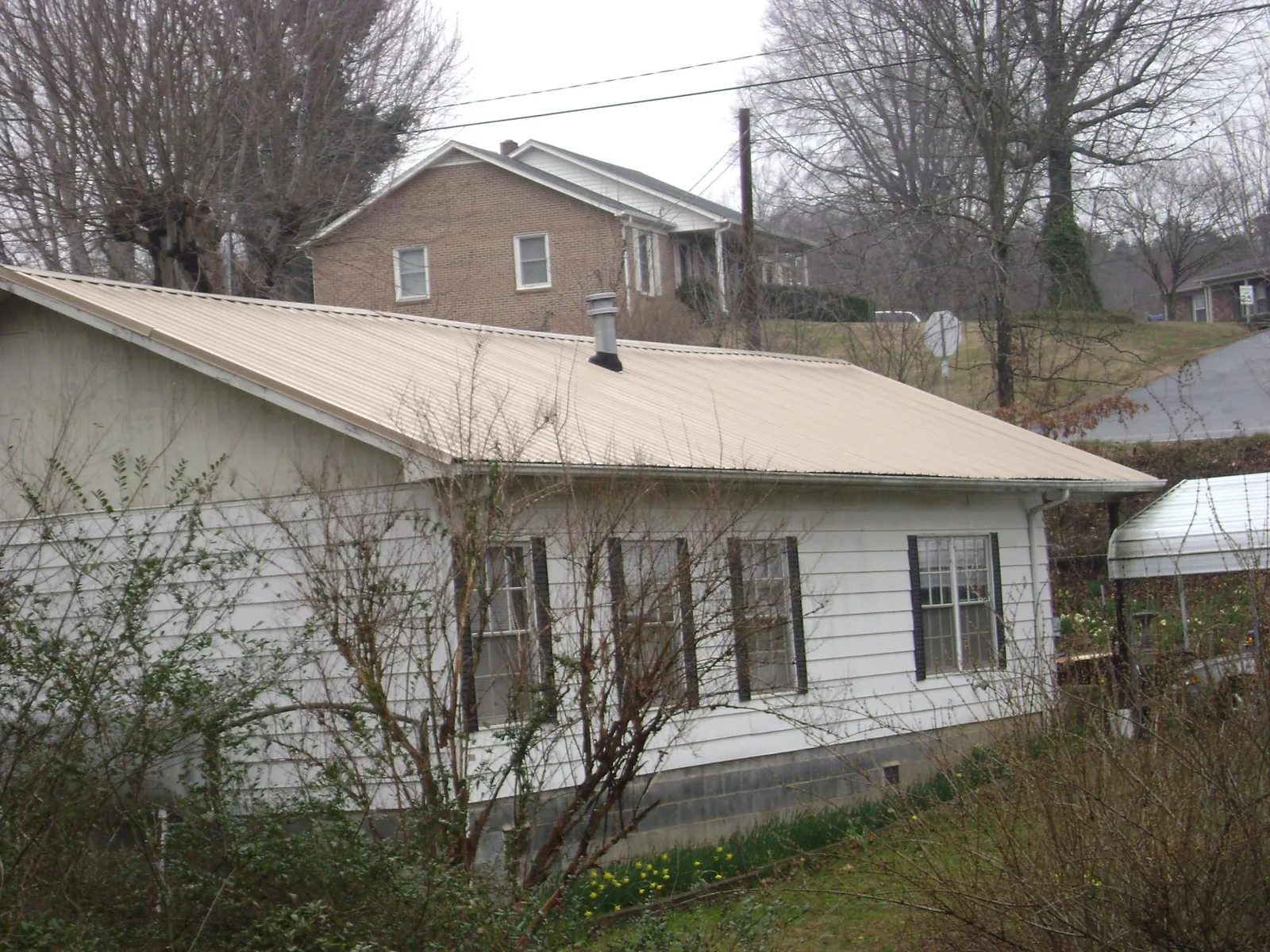 Tan metal roof on a white sided house set into a hillside — Commercial Roofing by Roofing Brothers in Prospect Park