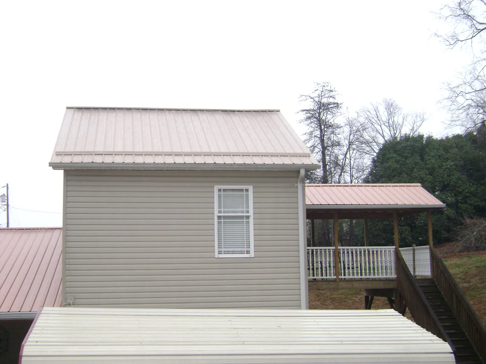 Tan metal roofs on a two story addition and attached porch, from a Roof Replacement job in Prospect Park